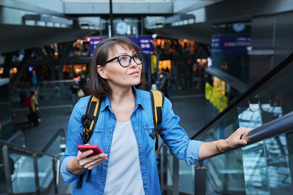 Frau auf der Rolltreppe mit Handy in der Hand, Geschäftsreisetrends






