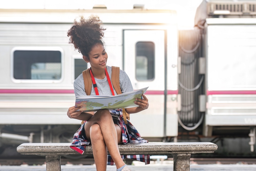 Frau sitzt auf einer Bank im Bahnhof und hält eine Karte, während sie auf einer Bleisure-Reise ist






