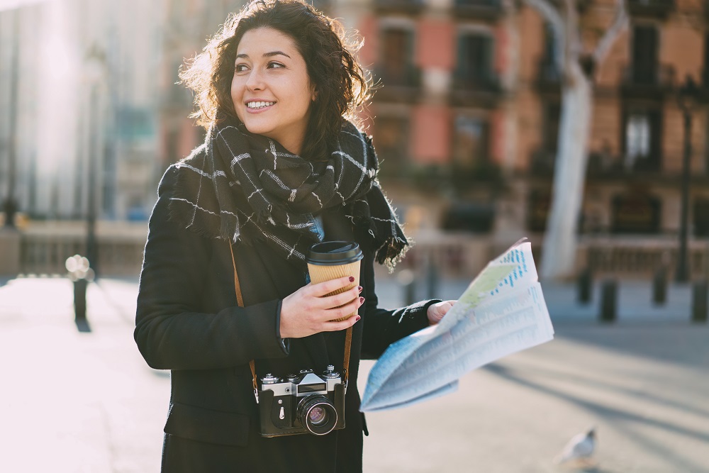 Girl visiting a city with camera, coffee and map in hand