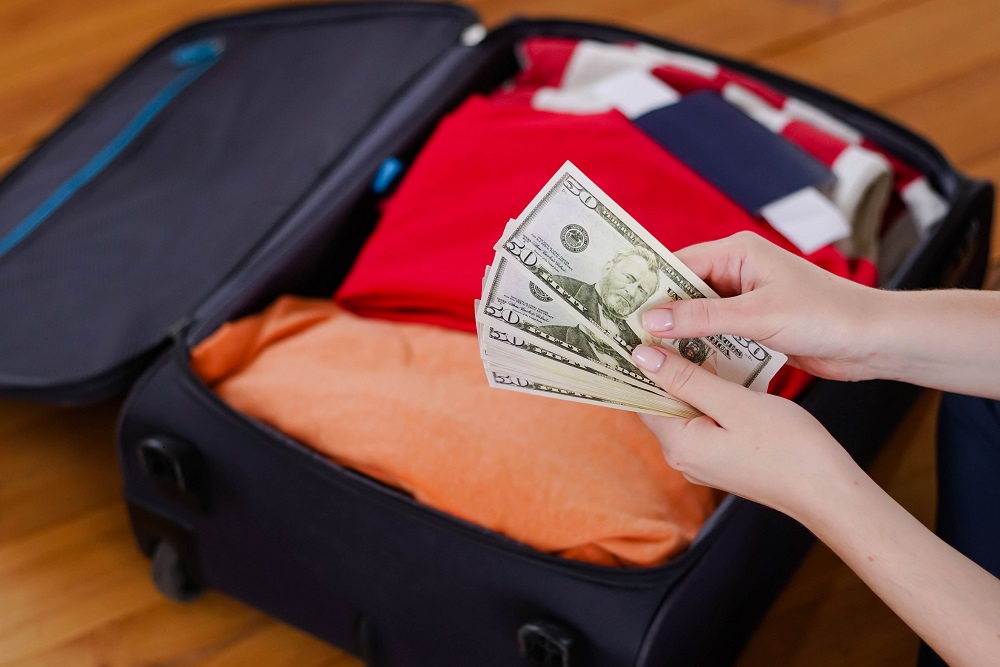 Woman's hands counting dollars in front of a packed suitcase