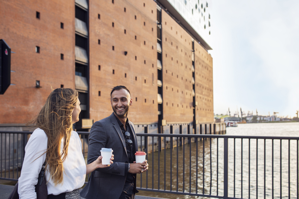 Man and woman walking on bridge by Elbphilharmonie and holding coffee cups